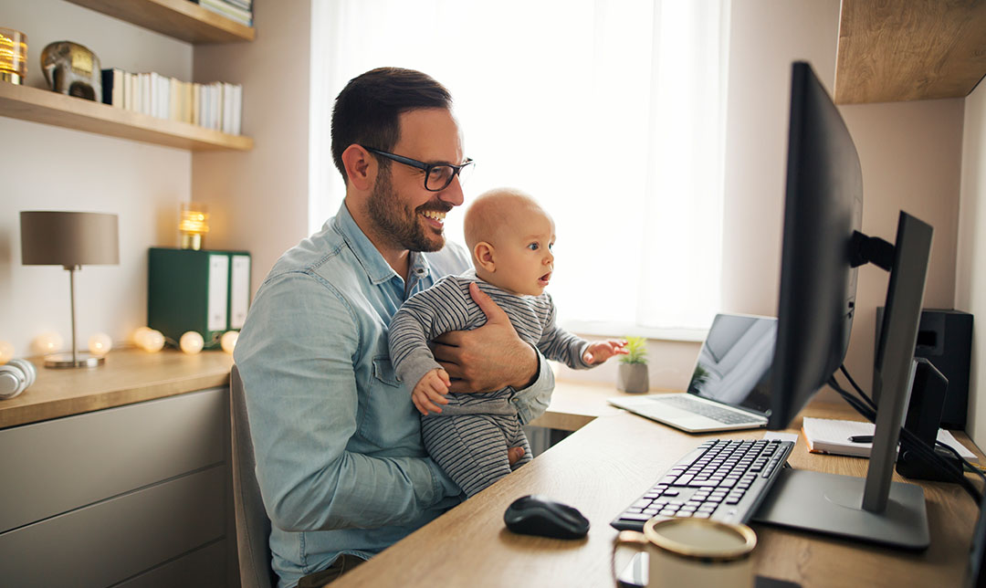 Man sat at a desk holding a child, they are both looking at a computer screen