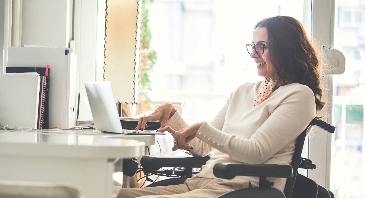 A woman with physical disabilities, smiles operating her laptop, signifying Royal Bank's dedicated support for people with accessibility.