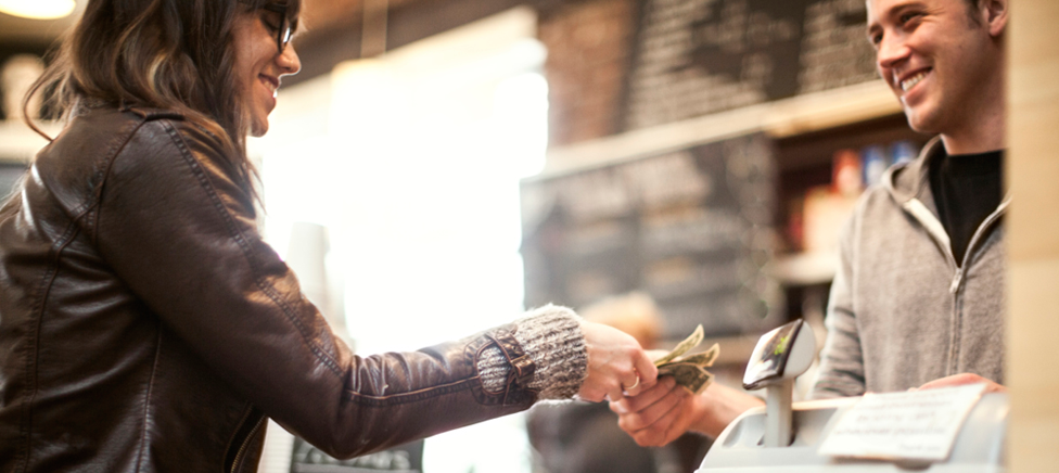 A hand passing over bank note to a smiling cashier.