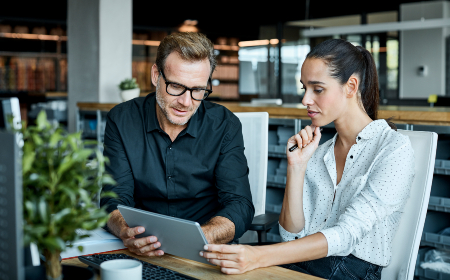 A man sat at his computer reading from a piece of paper. 