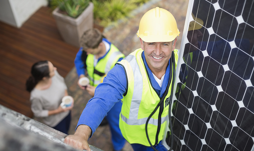 A person wearing a hi-vis and hard hat fitting a solar panel