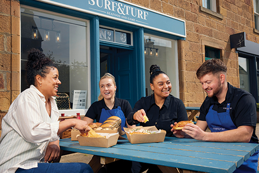 Business owners Lewis and Shona, enjoy great food and conversation with two staff, sat at a picnic table outside their successful eatery business, ‘Surf and Turf’