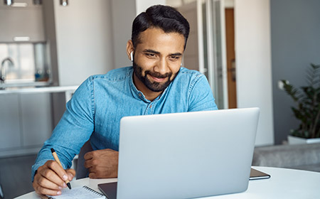 A man smiles, working at a laptop from home, signifying good investment outcomes, supported by Royal Bank commercial mortgages.