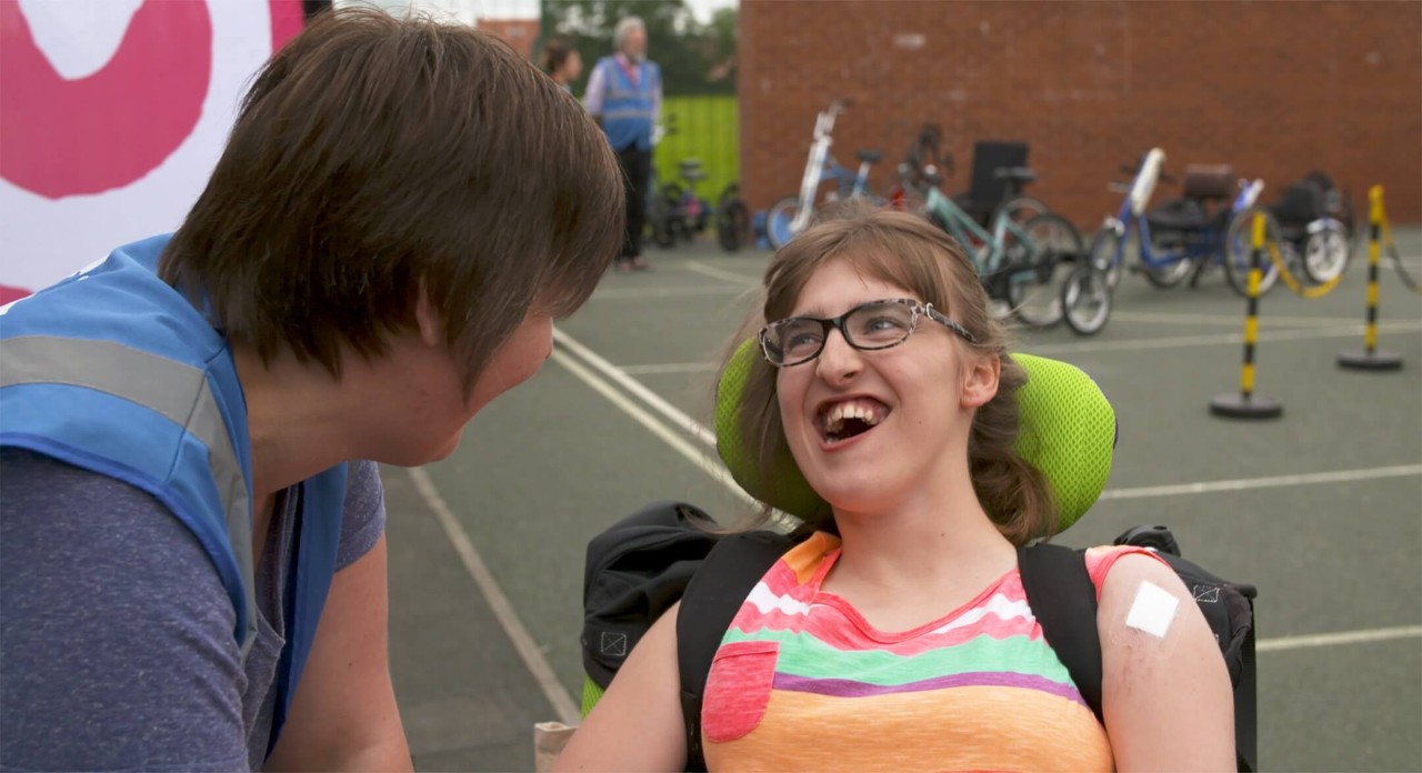 A young woman with disabilities is encouraged to ride an adapted bike.