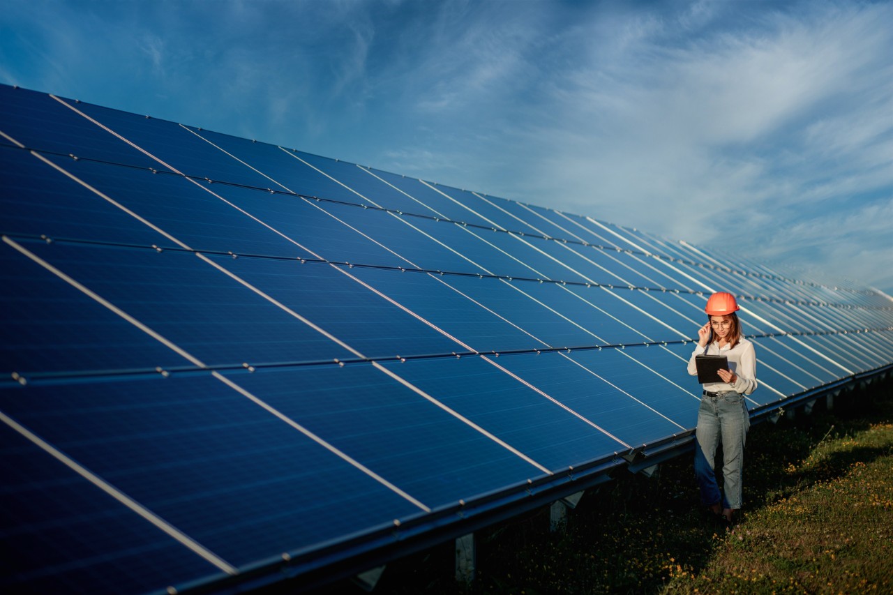 A woman wearing a hard hat standing next to solar panels.