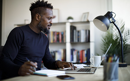 Somebody sat in an office, using a laptop while writing down notes