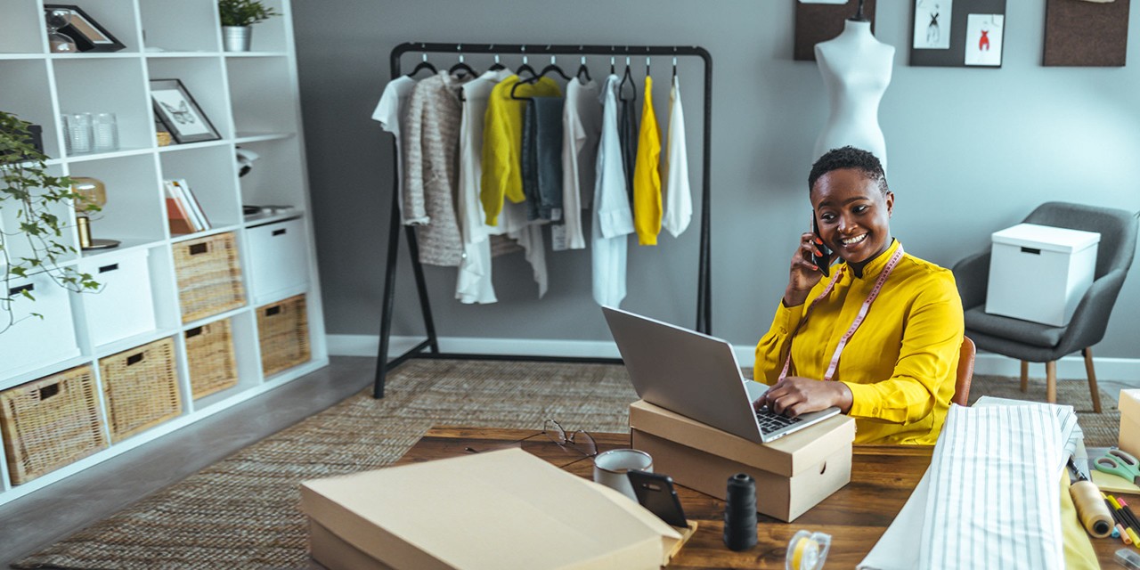 A business owner is sat smiling using her phone and laptop, signifying the ease with which Royal Bank credit card payments can be made.