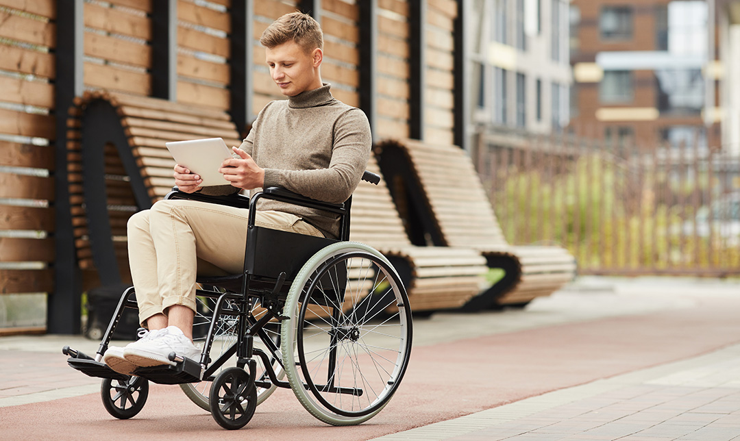 Person sitting in a wheelchair outdoors reading a tablet