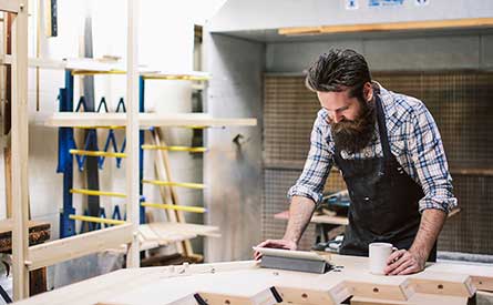 Person working in a workshop, smoothing a piece of wood on a workbench.