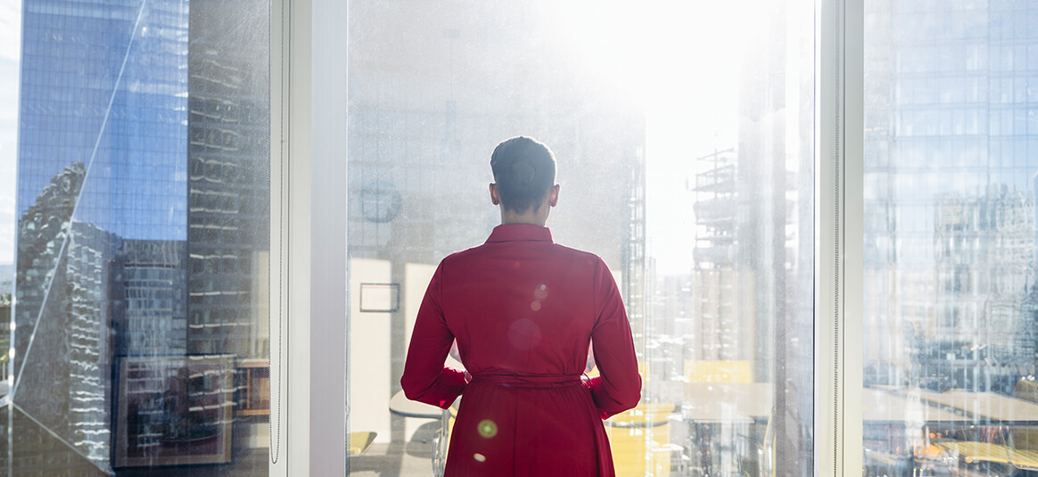 A business woman looks out of a skyscraper window, over the city below