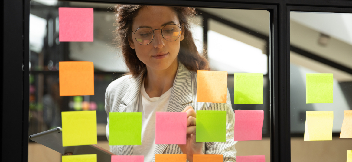 Photo of a woman writing on coloured post-it notes stuck to glass