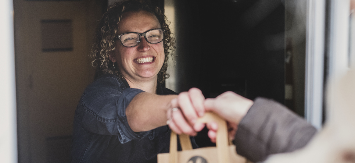 Photo of a smiling woman handing a paper bag to a customer