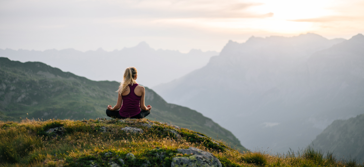 Photo of a woman meditating on a mountain peak