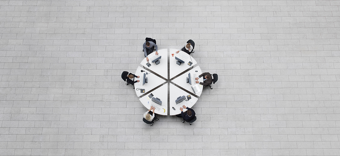 Top-down photo of office workers sitting at circular table split into six equal wedges
