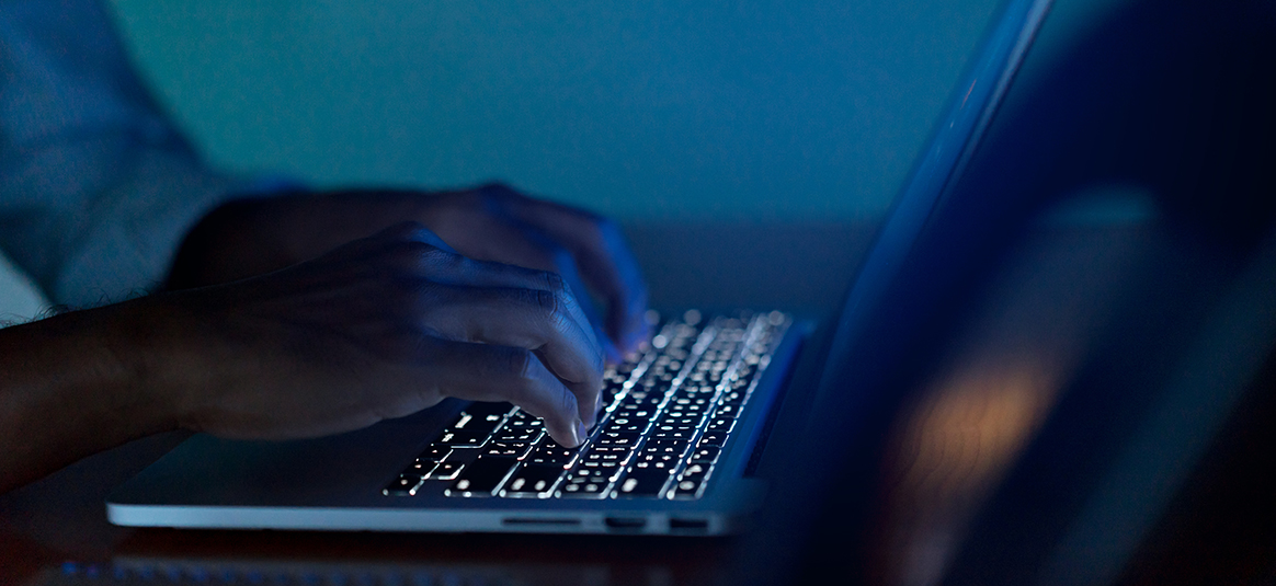 Photo of a person using a backlit keyboard in a dark room