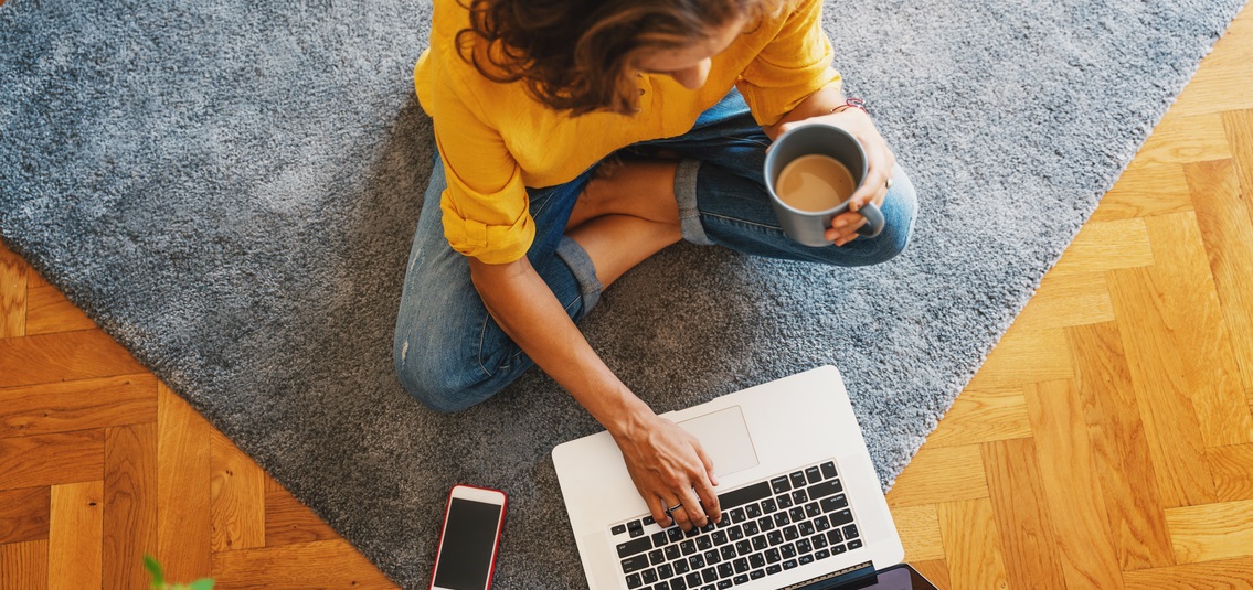 Woman sitting on floor with her laptop and a cup of coffee 