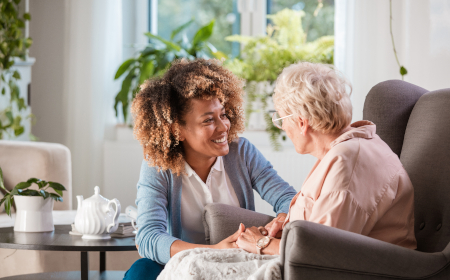 Older person sat in chair being cared for by young woman crouched beside her